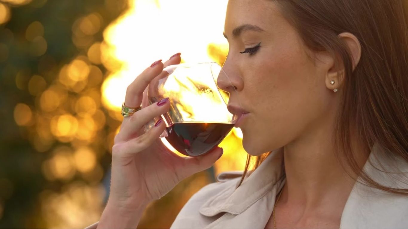 Woman holding an EQUILO glass at golden hour, just about to take a sip — warm sunlight and soft focus capture the elegance and emotion of the moment.