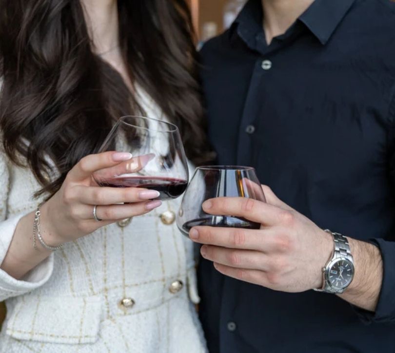 EQUILO No.2 glasses with red wine held side by side by a couple, close-up with only hands and glasses visible