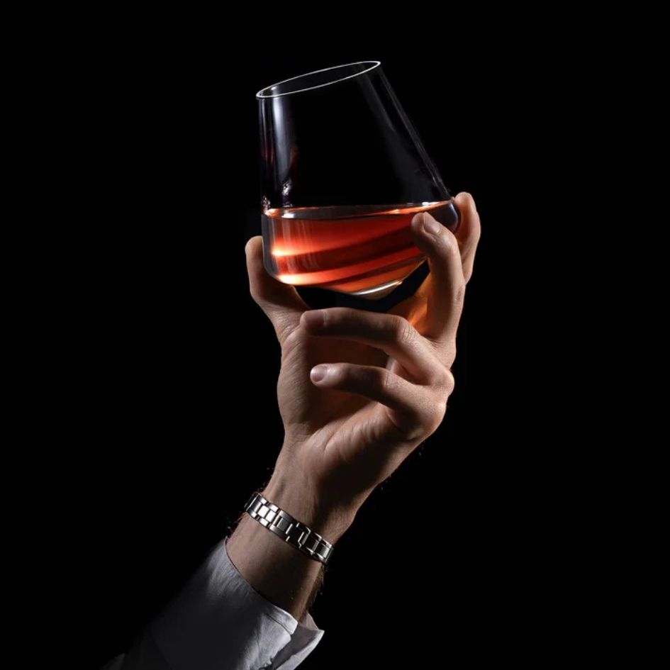 EQUILO No.3 glass held in hand with rich amber liquid against black background